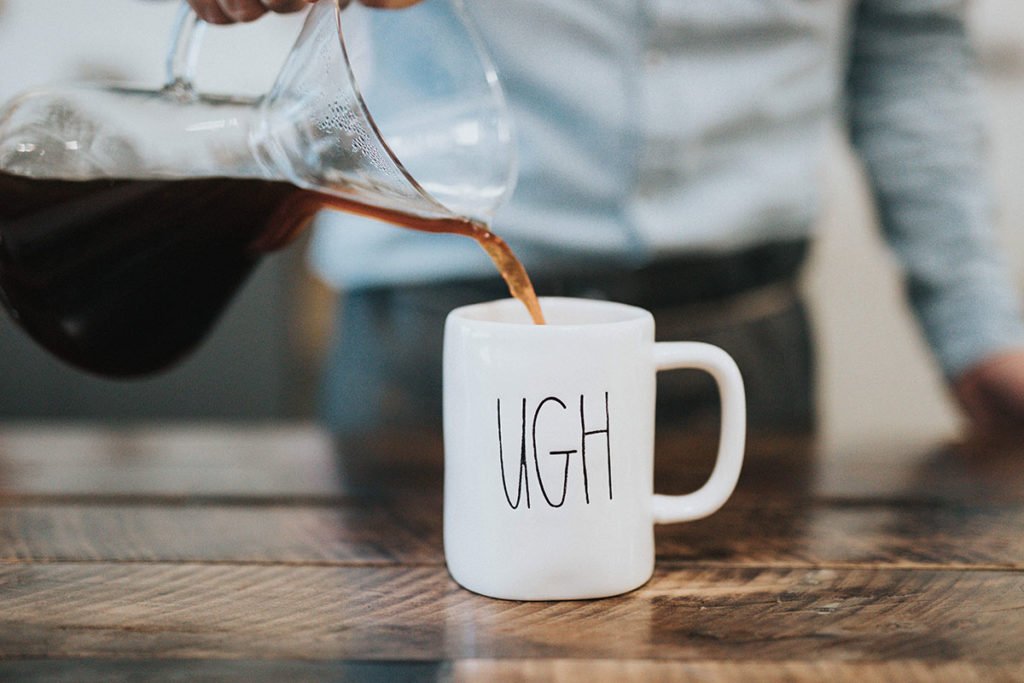 Image of a barista pouring coffee into a coffee mug that says'UGH'