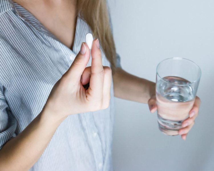 Image of a woman holding a glass of water taking probiotic supplement bifidobacterium longum in a pill