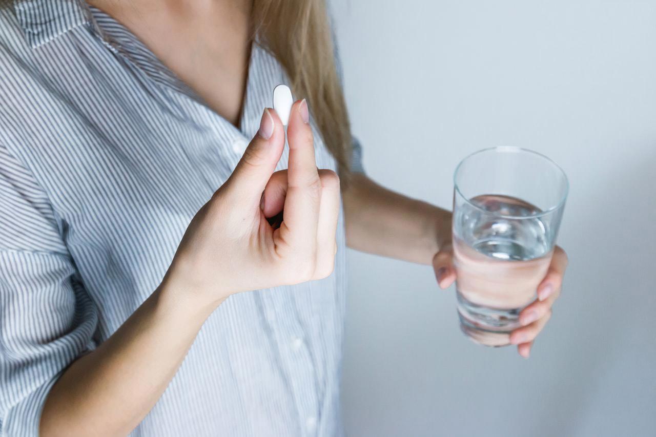 Image of a woman holding a glass of water taking probiotic supplement bifidobacterium longum in a pill