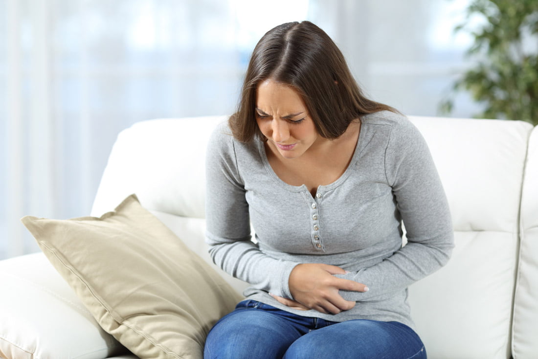 Image of a woman sitting down bending over in pain with her hands over her stomach from gastritis pain