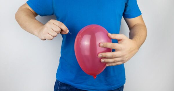 man with bloated stomach holding balloon and pin